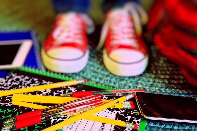 Kuvassa koululaisen tarvikkeita, kyniä, vihkoja, puhelin sekä punaiset tennarit.