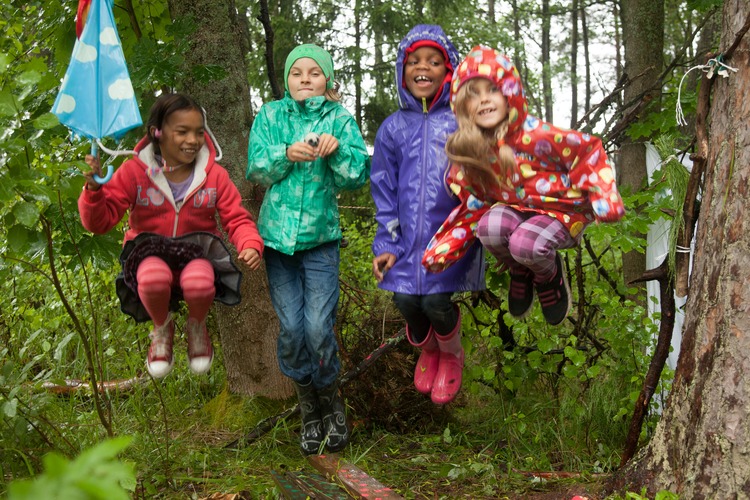 Neljä tyttöä hyppäävät ilmaan sateisessa säässä metsässä.